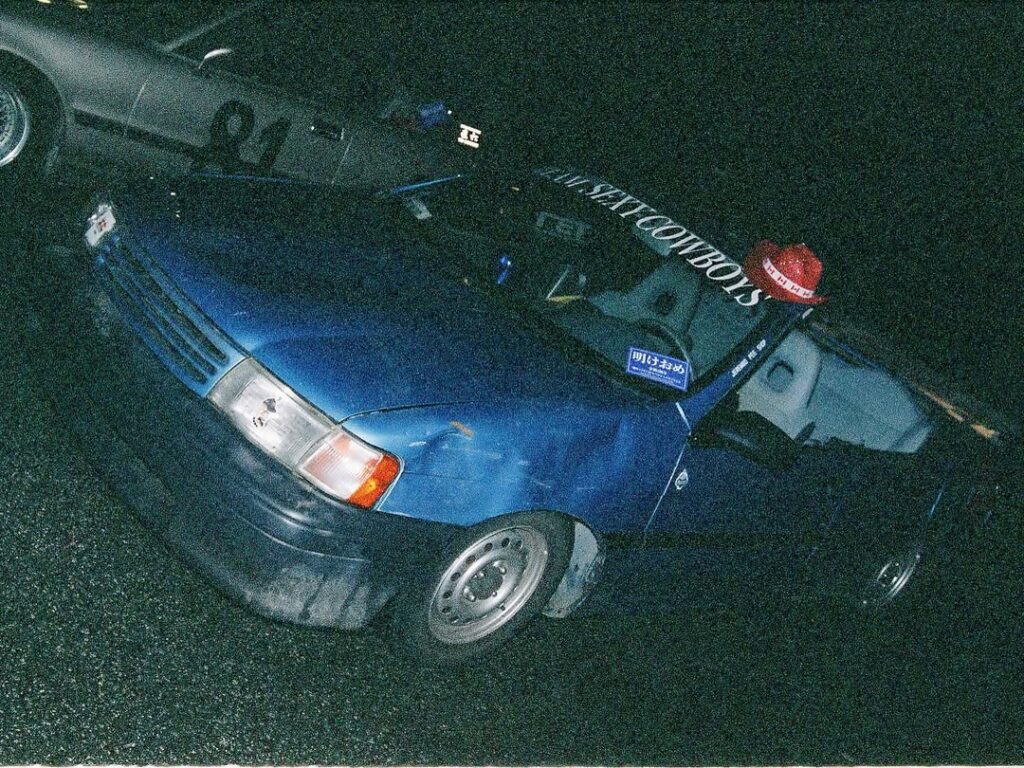 Old blue car at night with vintage design and custom decals, parked on wet asphalt.