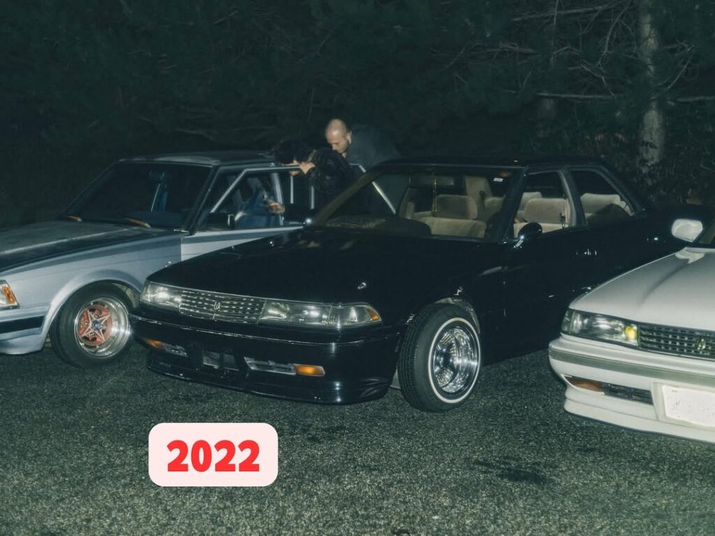 Vintage cars parked at night with people in the background, marked 2022 in the foreground.