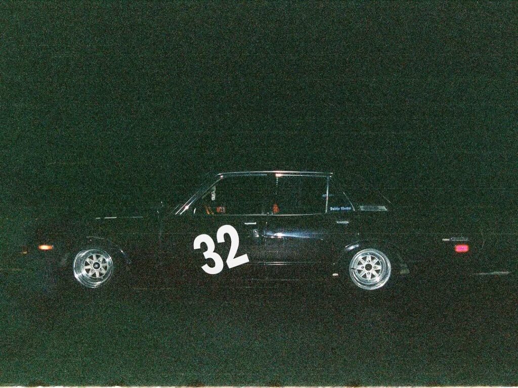 Race car with number 32 on side, parked at night with dark background, showcasing sleek wheels and sporty design.