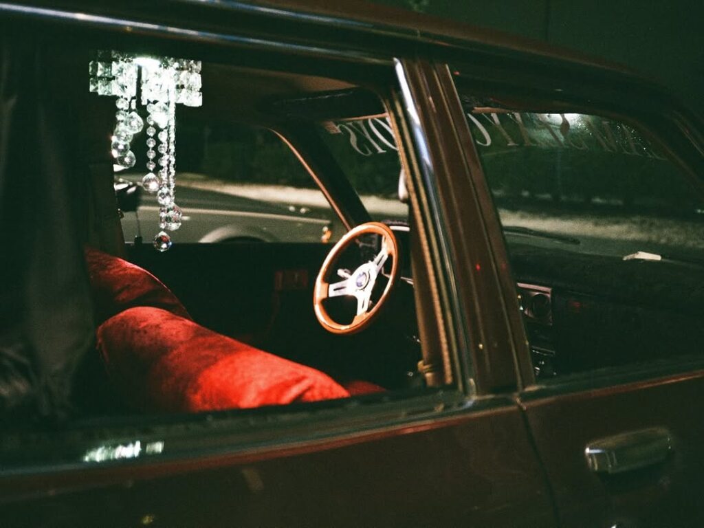 Vintage car interior with red seats, chandelier, and wooden steering wheel at night.