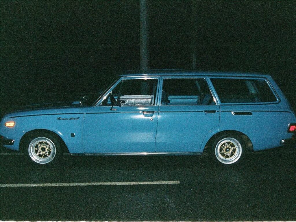 Vintage blue station wagon parked at night, side view. Classic car with unique wheels.