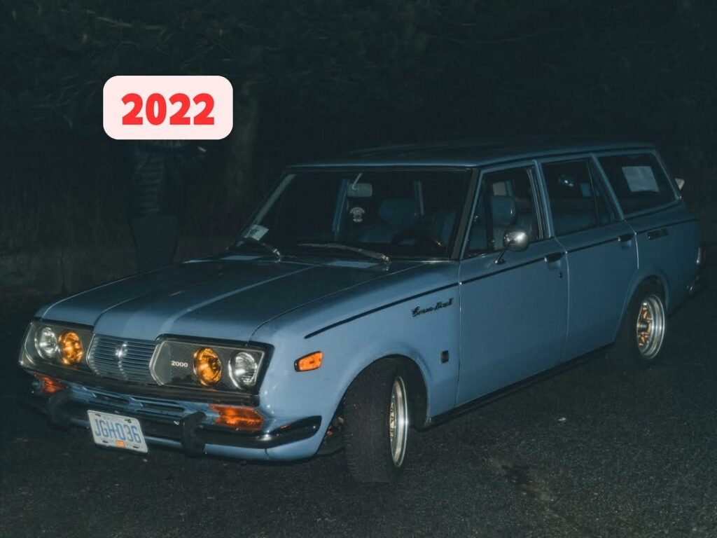 Classic blue car with amber lights in a night scene, dated 2022, parked under dim lighting.