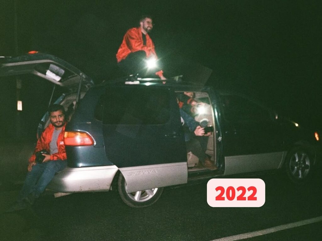 People in red jackets with cameras gather around a van at night, 2022.