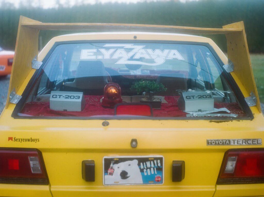 Yellow Toyota Tercel rear, adorned with decals and a polar bear license plate, GT-203 boxes inside.