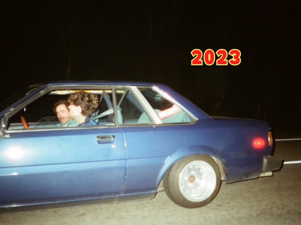 Two people in a vintage blue car driving at night, with the year 2023 displayed above.