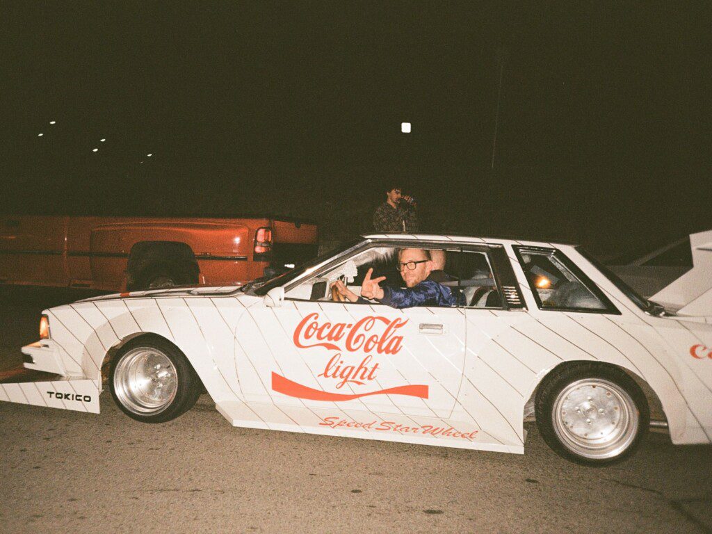Vintage car with Coca-Cola branding and a driver at night, showcasing retro automotive style.