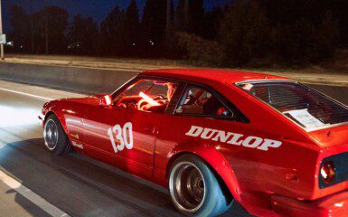 Red sports car with number 130 racing on highway at night, featuring Dunlop branding on the side.