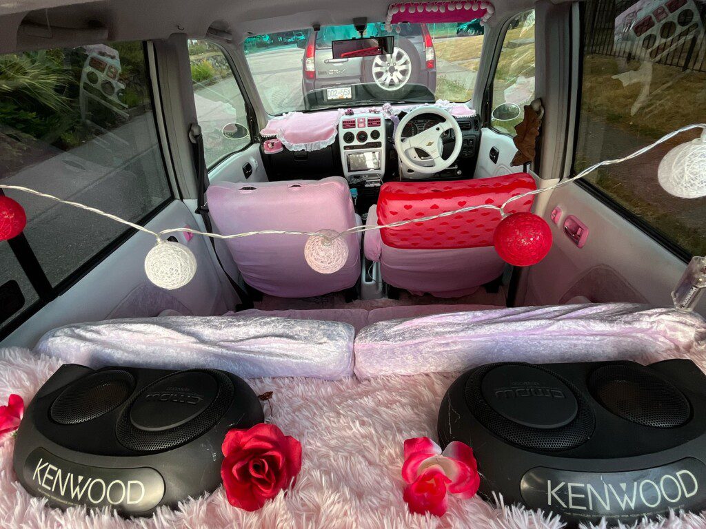 Cozy car interior with pink decor, Kenwood speakers, and string lights showcasing a personalized and stylish setup.