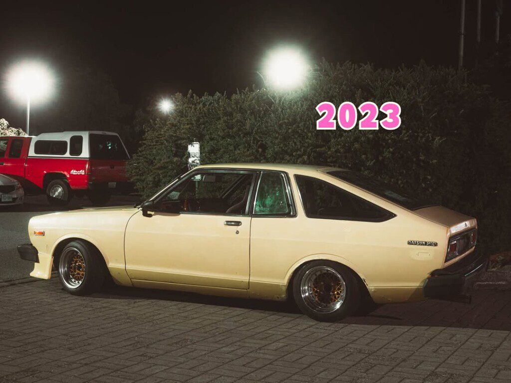 Vintage Datsun 210 parked at night with glowing headlights and a retro vibe, labeled 2023 in bold text.