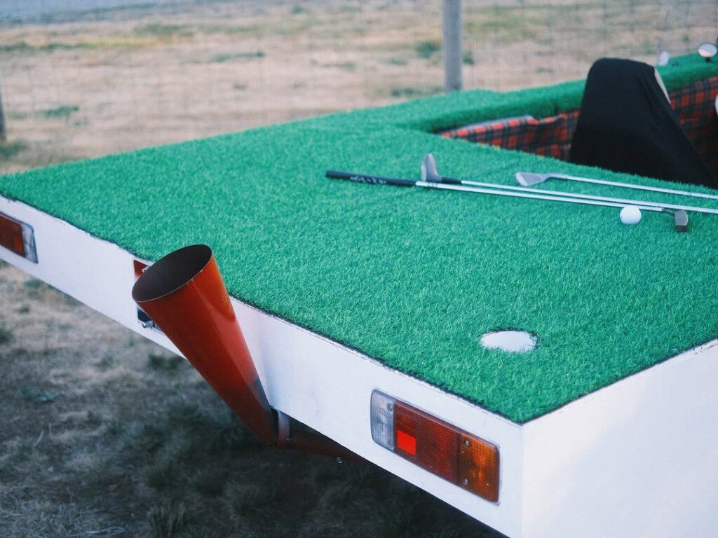 Golf clubs and ball on a unique green-covered truck bed, resembling a mini golf putting course.